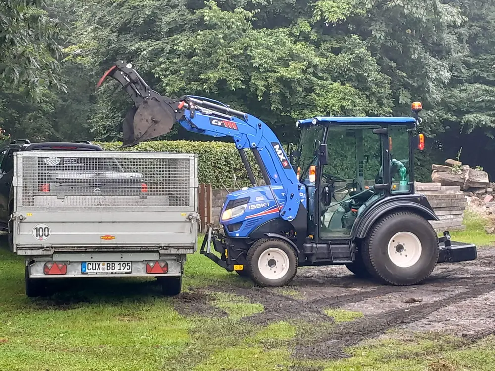 Iseki Traktor mit Frontlader belädt einen Kipperanhänger