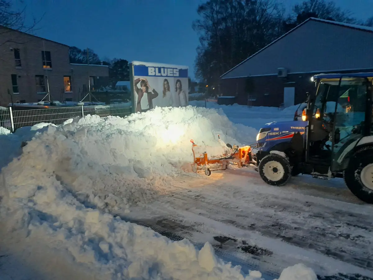 Traktor schiebt einen Schneeberg auf einem geräumten Parkplatz zusammen
